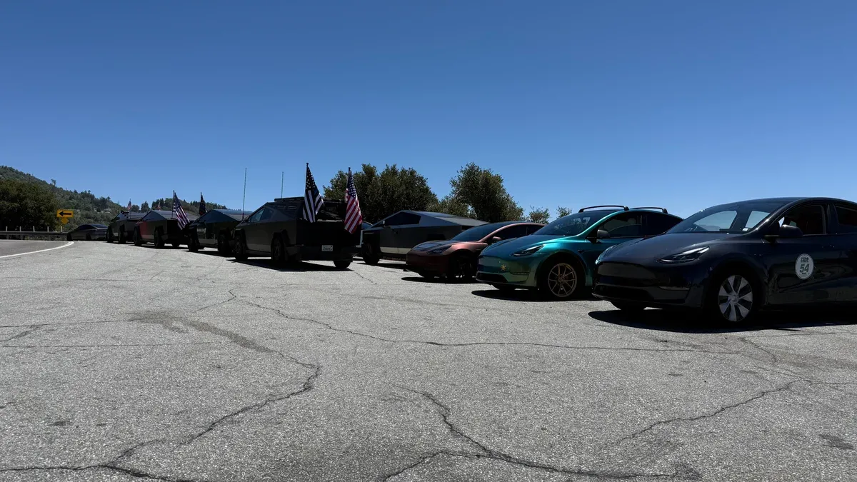 Line of Teslas including Cybertrucks with American flags on a scenic mountain road above the clouds