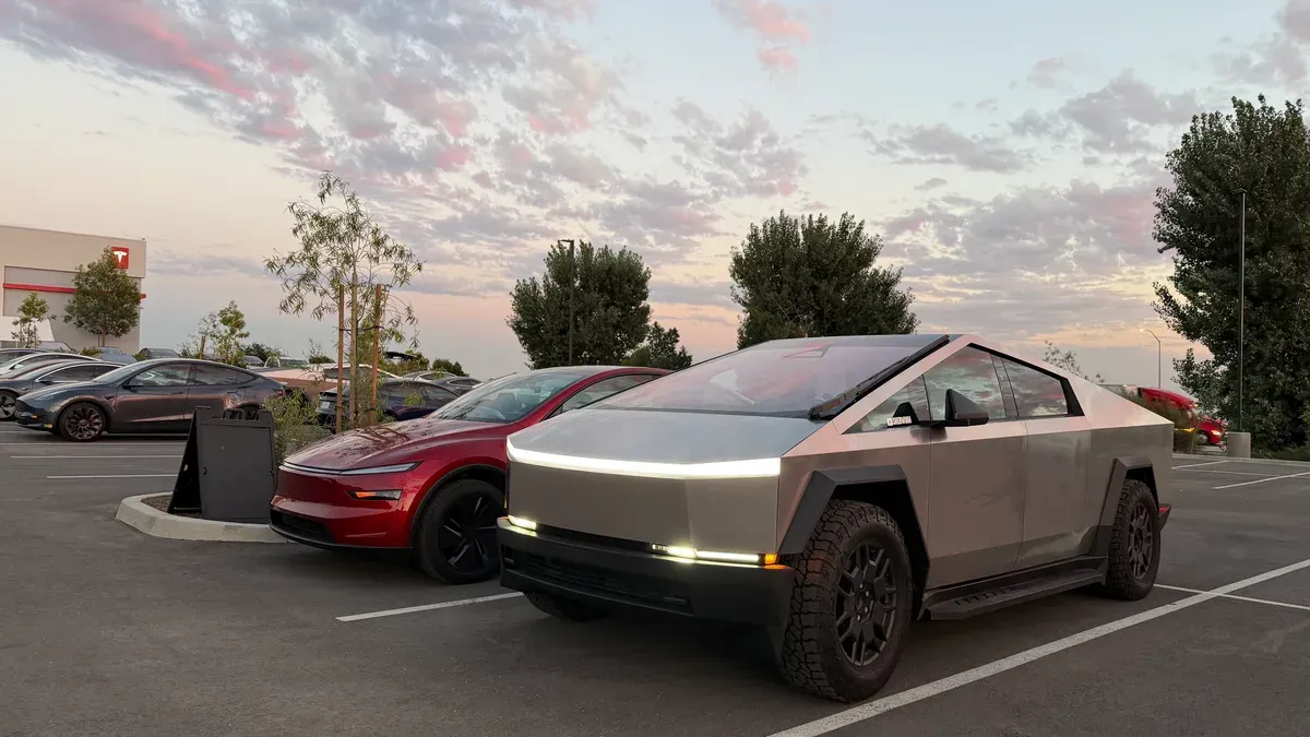 Silver Tesla Cybertruck and red Lucid Air parked side by side at sunset outside a Tesla service center