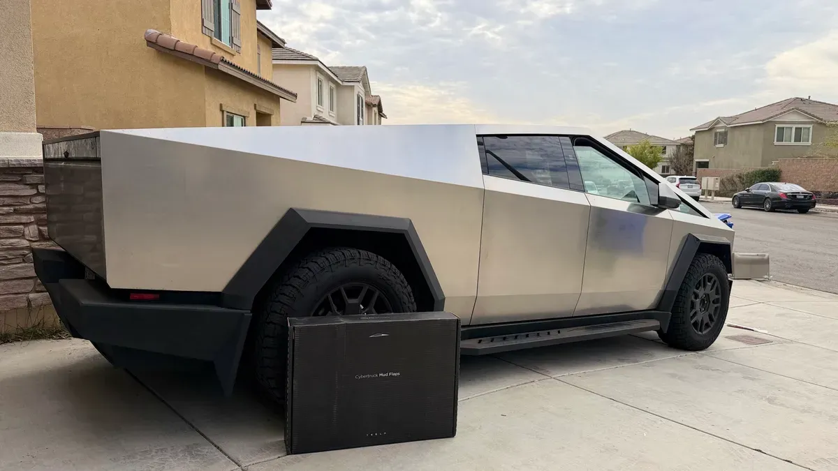 Tesla Cybertruck parked on a driveway with a box of Cybertruck mud flaps in front of the rear wheel.