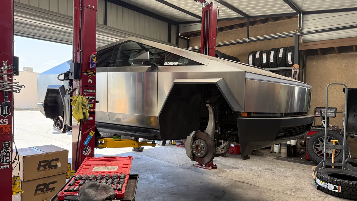 Tesla Cybertruck lifted on a red two-post lift in a garage, front wheel removed, tools on floor.