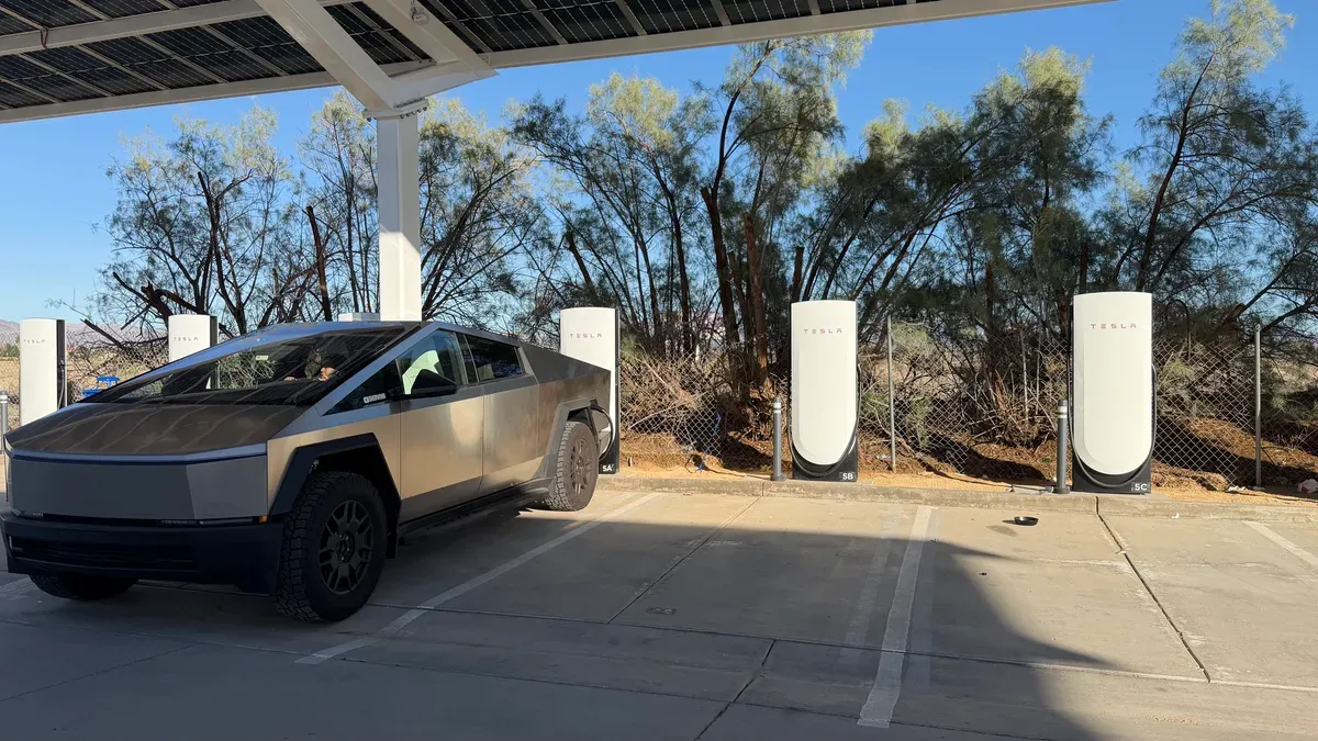 Tesla Cybertruck charging at a Supercharger station with solar canopy in the desert.