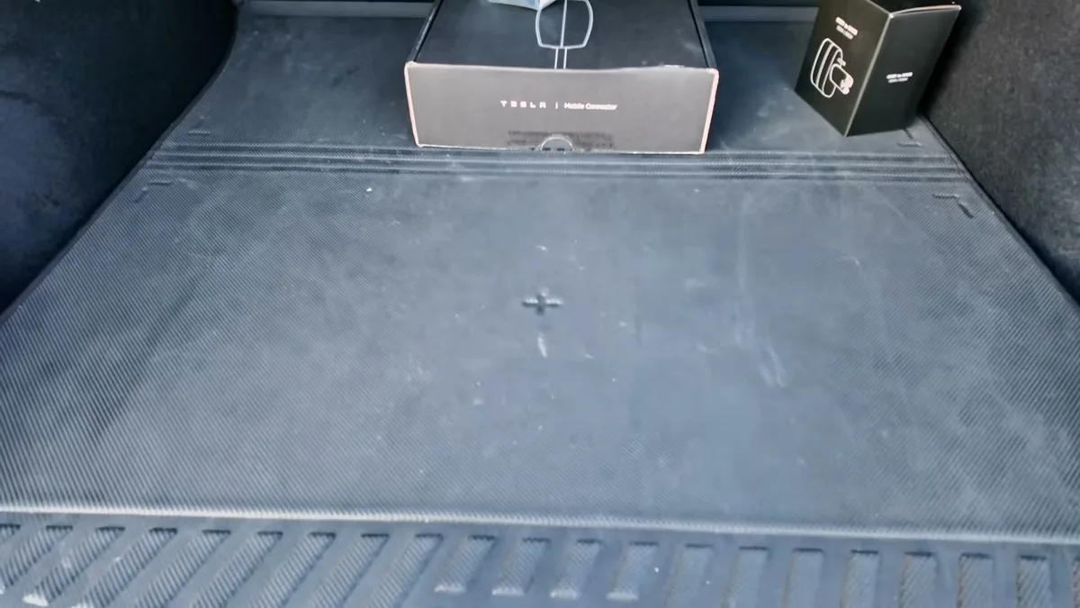 Black textured trunk liner covering the Model Y Juniper cargo area with the mobile connector visible