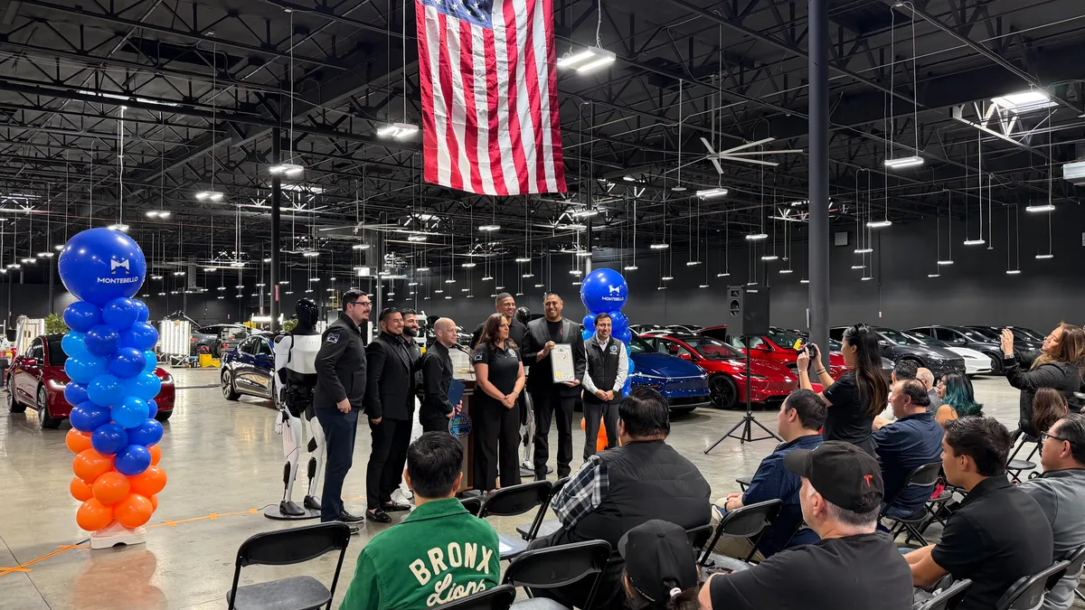 Presentation stage with two Optimus units and a large American flag at the Tesla Montebello grand opening.