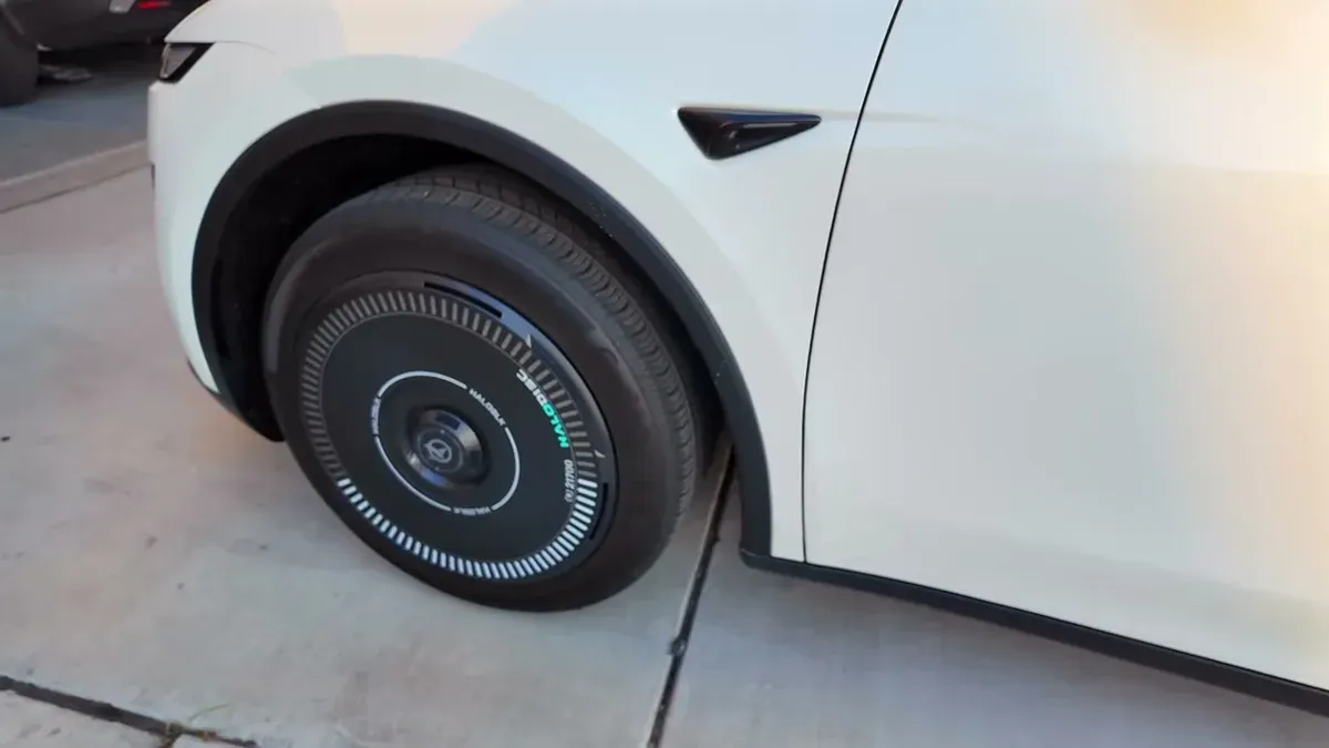 Close-up of white Tesla front wheel with black HALONIC aero cover on concrete driveway.