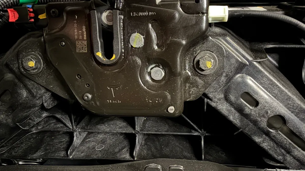 Close-up of the Tesla frunk latch mechanism with yellow-marked bolts and Tesla logo