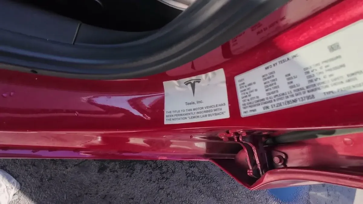 Close-up of Tesla door jamb sticker reading LEMON LAW BUYBACK on glossy red Model 3
