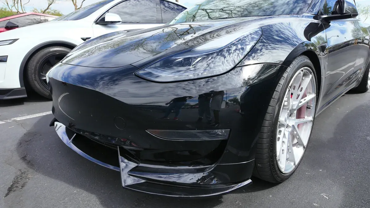 Black Tesla Model 3 Performance with an aftermarket front lip and white Signature wheels, lowered about an inch and a half