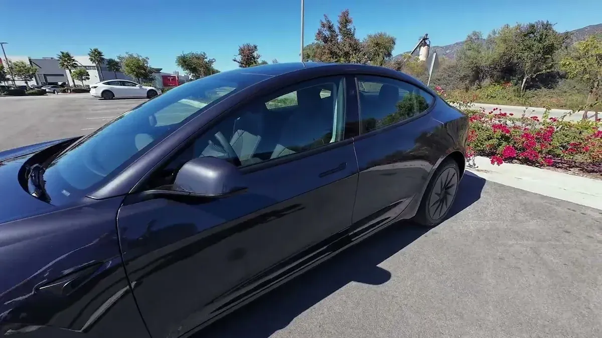 Low angle side profile of the Model 3 Standard, tinted glass and Cybertruck visible in background