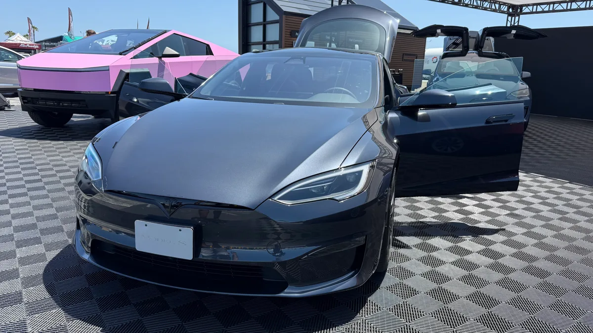 Dark grey Tesla Model S Plaid with doors open on a checkered display floor, pink Cybertruck visible in the background at Electrify Expo