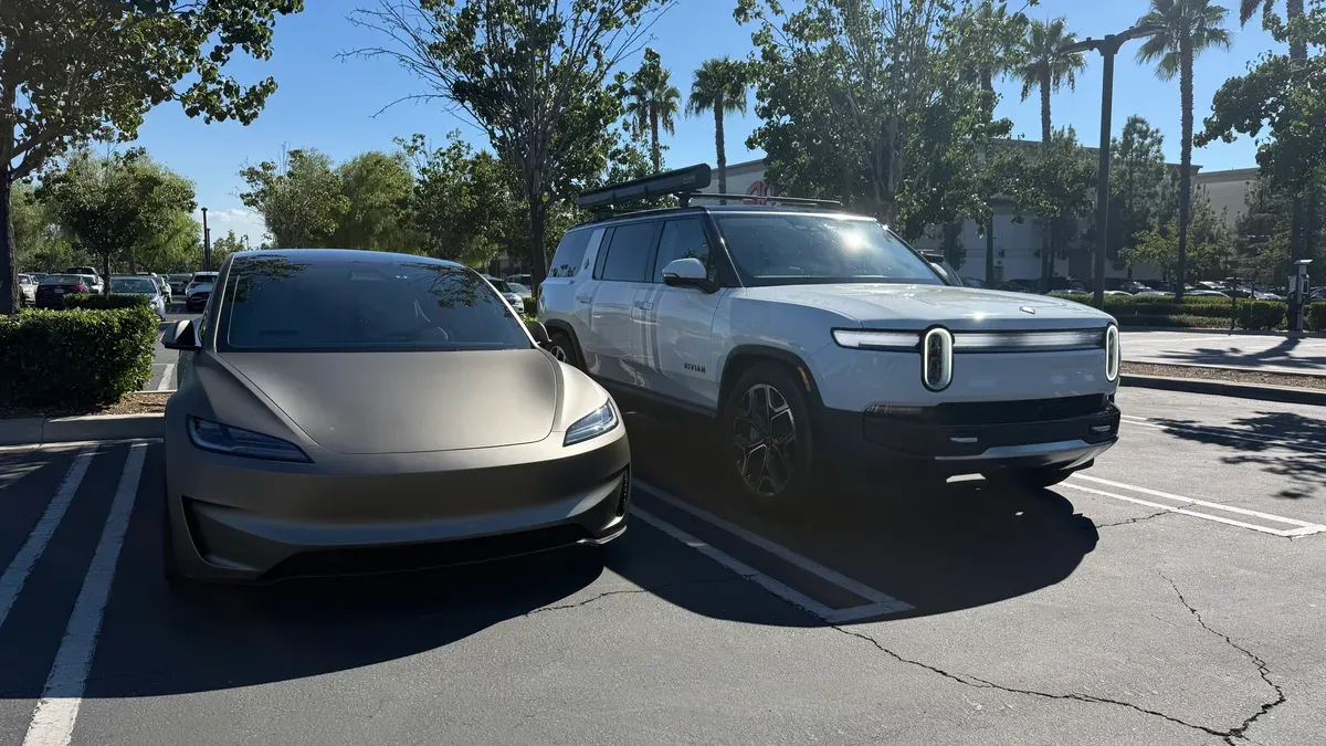 Matte bronze Tesla Model S and white Rivian R1S parked side by side under blue sky with palm trees