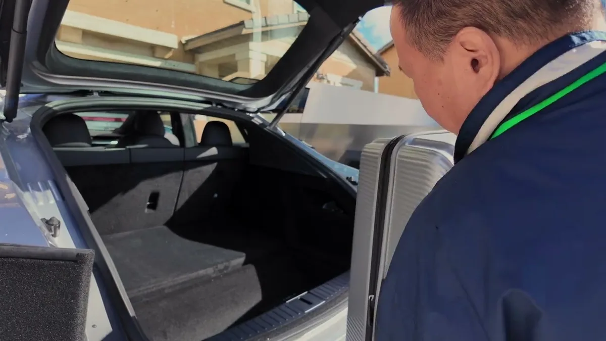 Man loading a silver suitcase into the open trunk of the 2026 Tesla Model S.