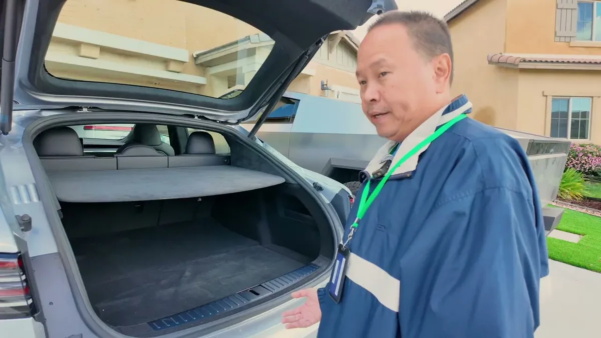 Man standing next to the spacious open trunk of the 2026 Tesla Model S, Cybertruck in background.