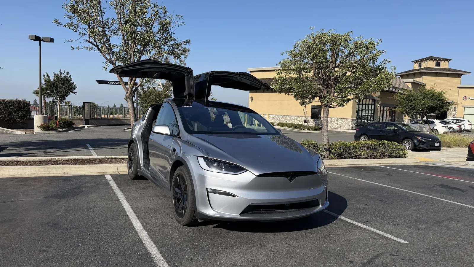 Silver Tesla Model X with both falcon wing doors raised in a parking lot.