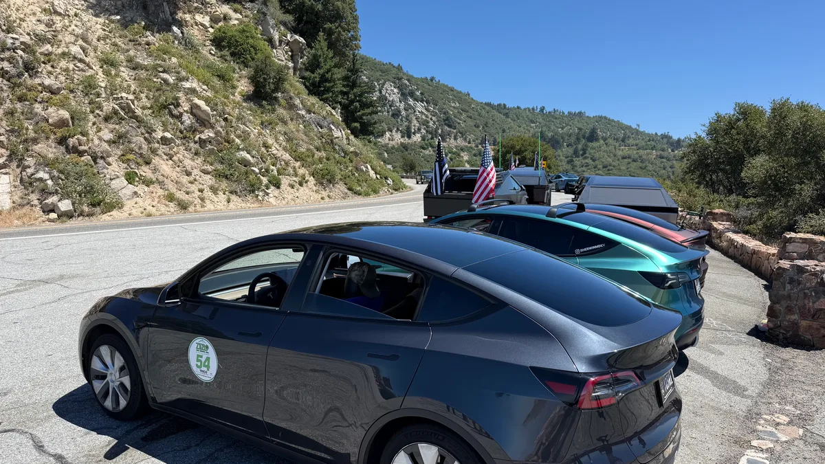Dark gray Tesla Model Y with TESLA 54 rear window sticker parked on a mountain road with flags in background