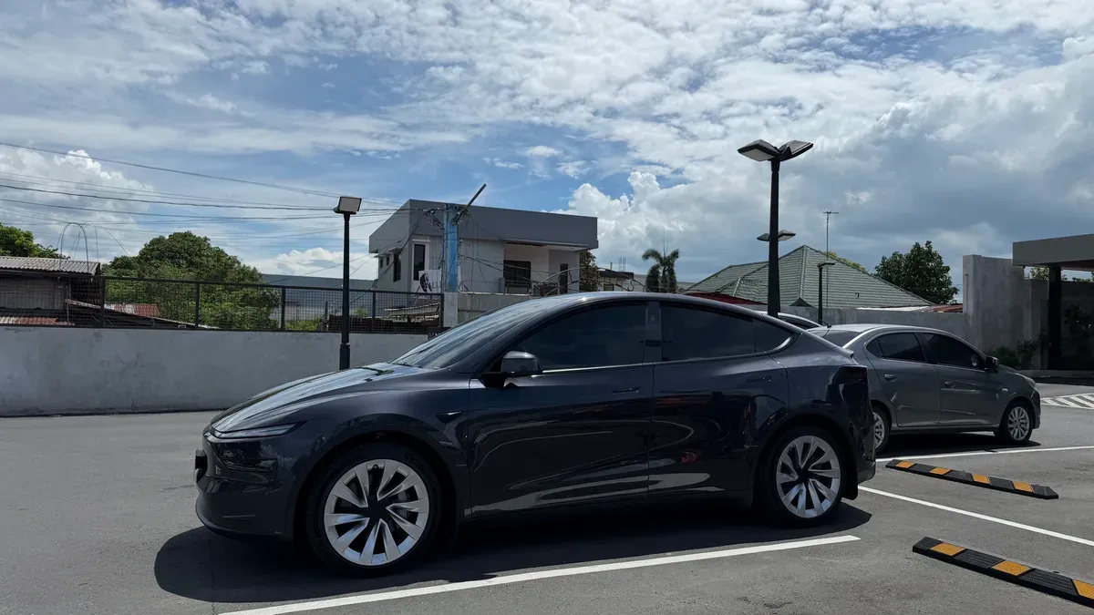 Angled side view of a Stealth Gray Tesla Model Y parked outside a Starbucks in Santa Cruz, Laguna