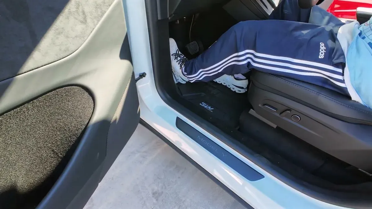 Person's feet in white sneakers resting on the installed 3W floor mat in the driver's side of a white Tesla Model Y