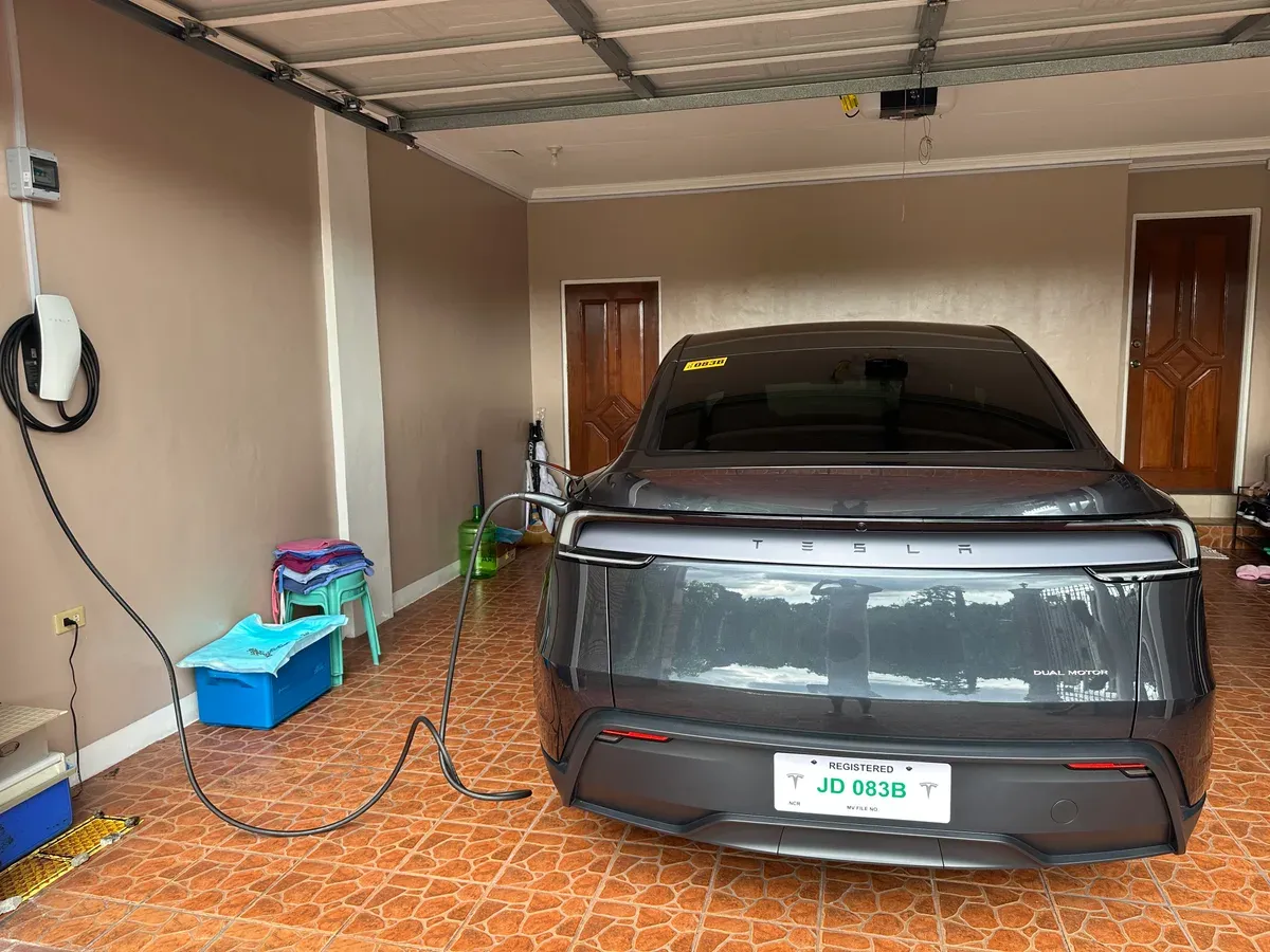 Stealth Gray Tesla Model Y plugged into a Tesla Wall Connector inside a home garage in the Philippines
