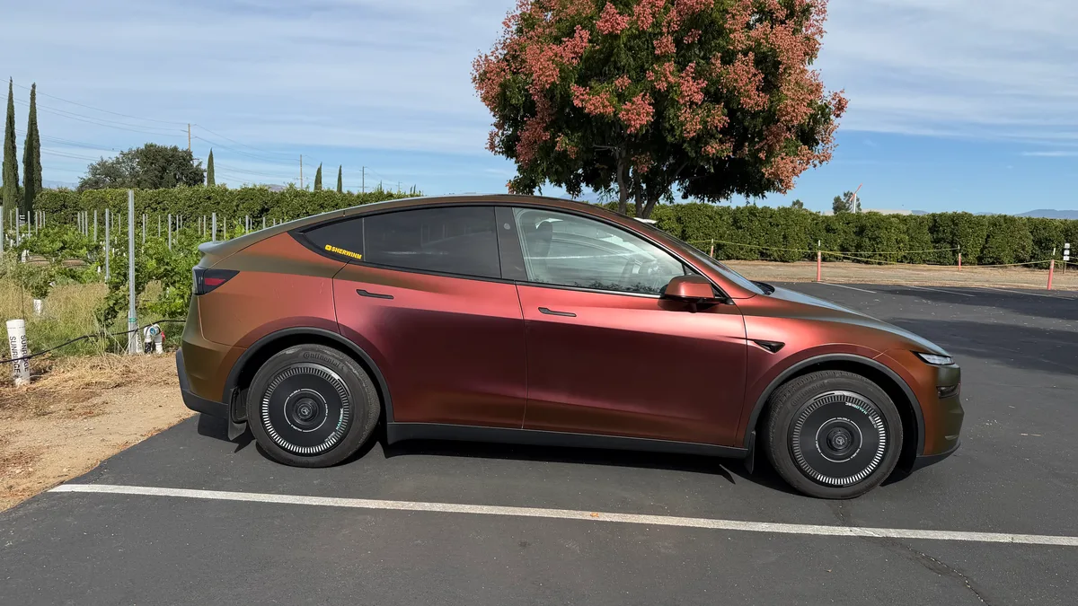 Side profile of the Model Y Juniper in Rising Sun wrap at the vineyard, deep copper tones, SHERWINM sticker visible
