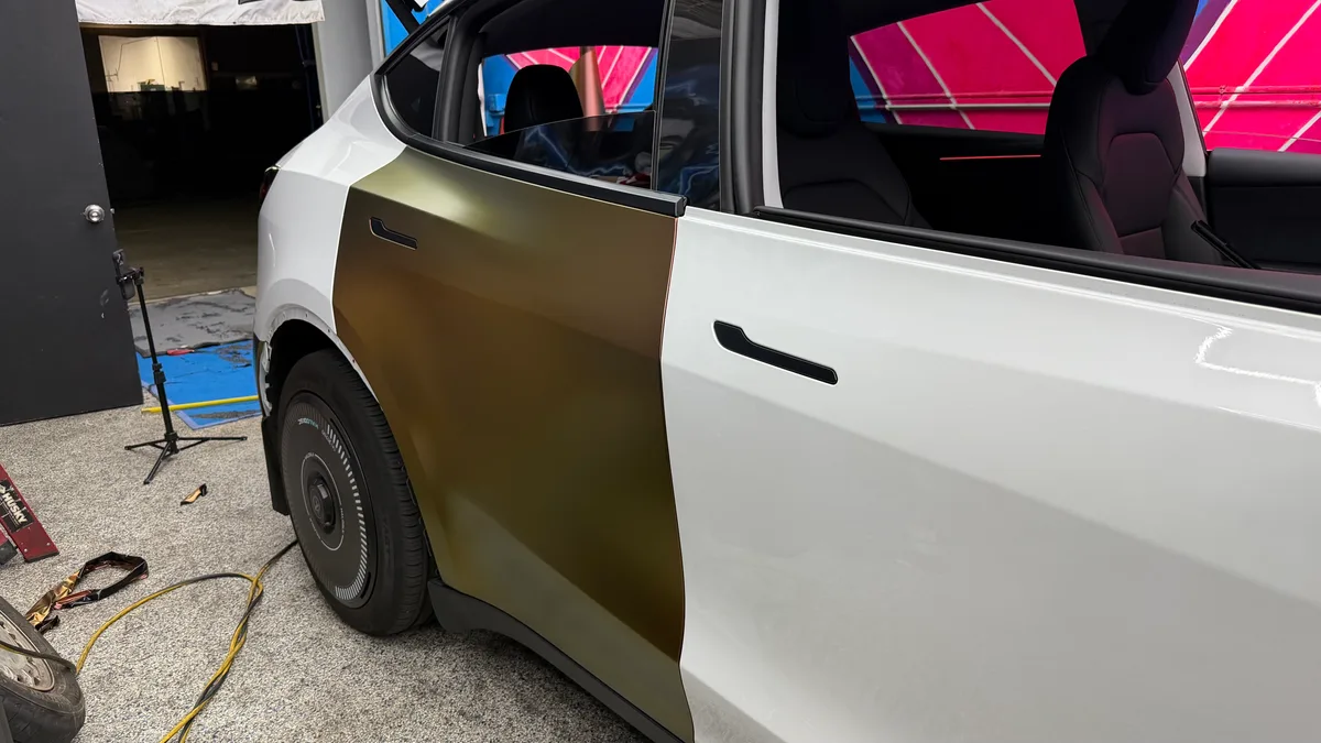 Side view of Model Y mid-wrap, rear half in gold-olive Rising Sun film contrasting with the untouched white front door