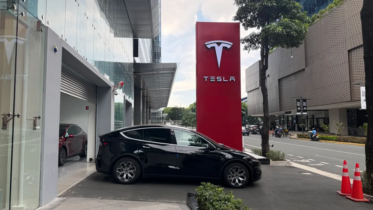 Black Tesla Model Y parked outside the modern BGC Tesla showroom with a large red Tesla logo sign.