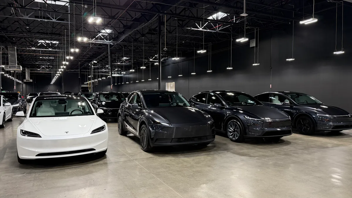White Tesla Model Y parked in front of a row of dark Teslas inside the Montebello showroom.
