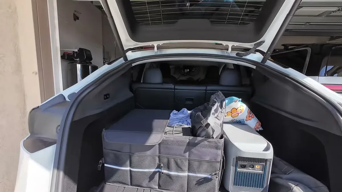 Tesla Model Y trunk with black organizer holding power station, Starlink, and accessories, dog peeking from rear seats