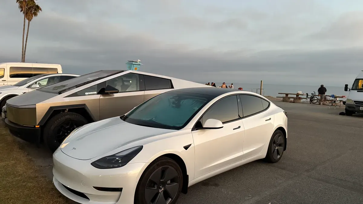 White Tesla Model 3 and Cybertruck parked near the ocean at Dana Point with people on the beach in the background