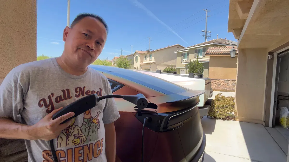 Sherwin holding the Gen 3 Mobile Connector with the Tesla Outlet Adapter on the end, plugged into the charge port of his color-shift wrapped Model Y Juniper