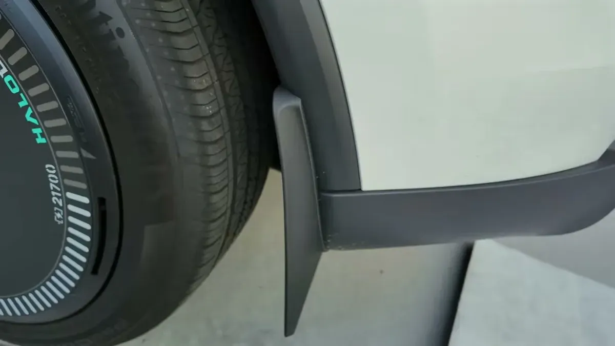 Newly installed black mud flap on white Tesla's rear wheel well with aero cover.