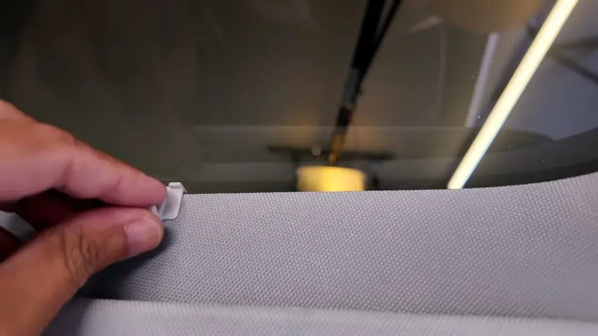 Close-up of hand attaching a white clip to the edge of a gray fabric roof shade during installation in a Tesla