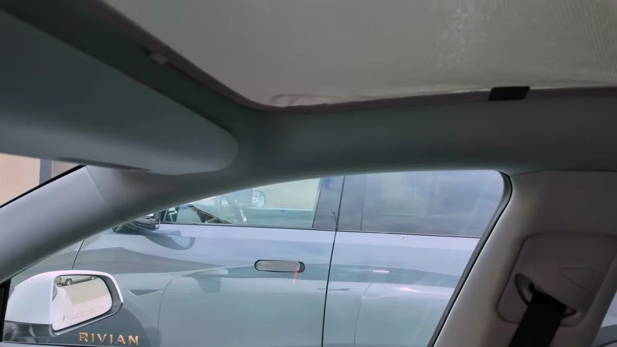 Interior view of a Tesla roof with gray Jowua sunshade installed across the panoramic glass, Rivian visible through side window