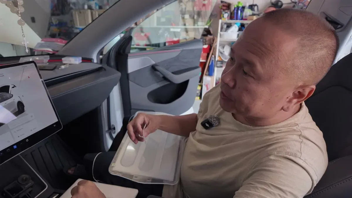 Man in Tesla passenger seat holding clear screen protector over central display, preparing for installation