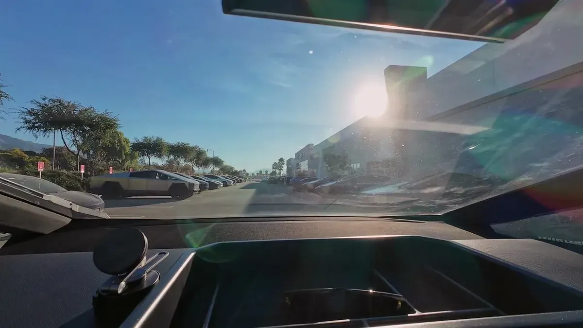 View from inside the Cybertruck pulling into the Tesla service center lot with several Cybertrucks visible in bright sun