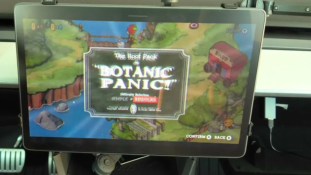 Tesla touchscreen showing Cuphead's Botanic Panic boss fight with two players — carrot and giant boss visible