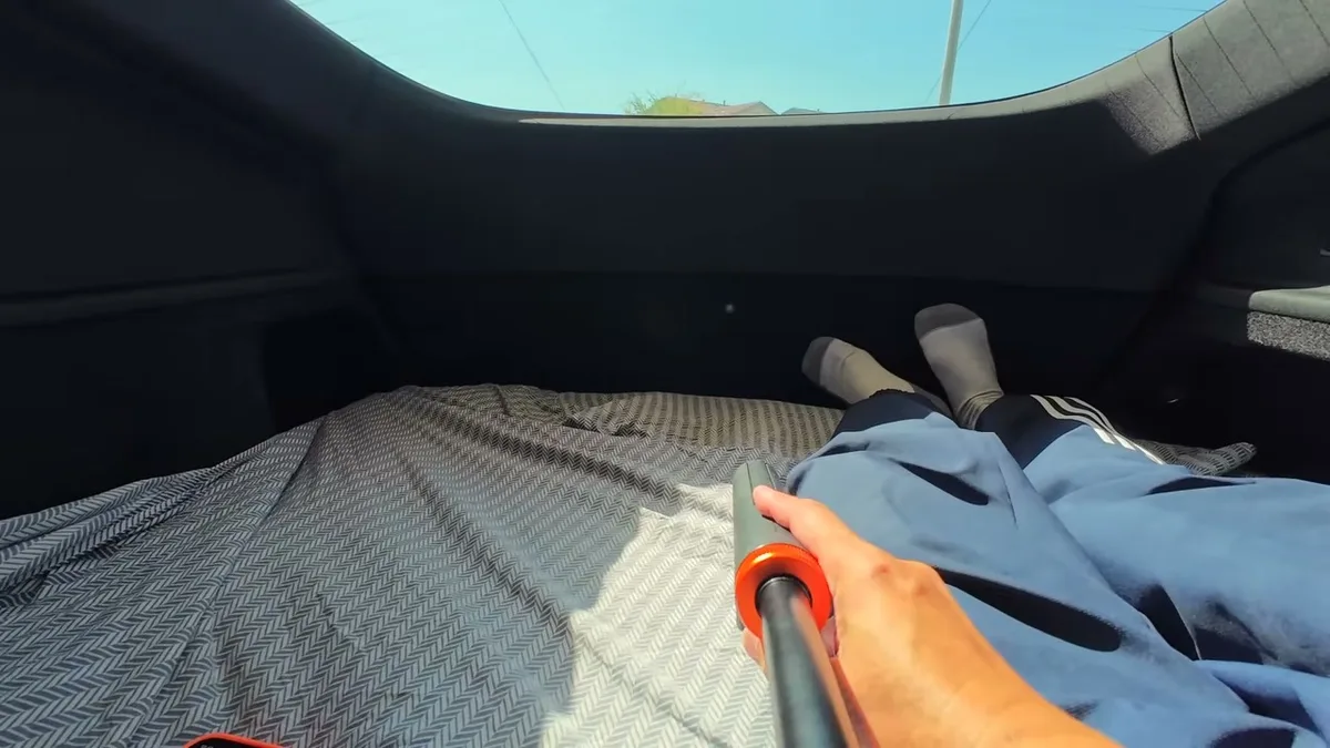 First-person view from inside Tesla trunk lying on patterned bed sheet with legs stretched out
