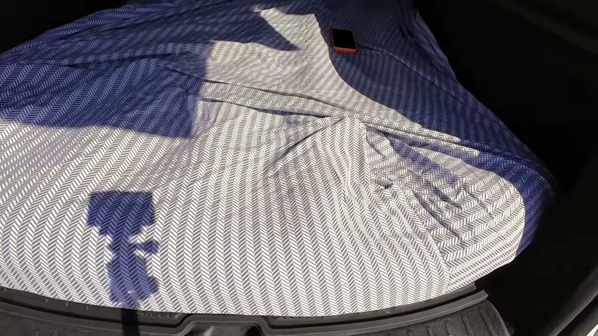 Overhead view of herringbone bed sheet covering the full Tesla trunk with a phone resting on top