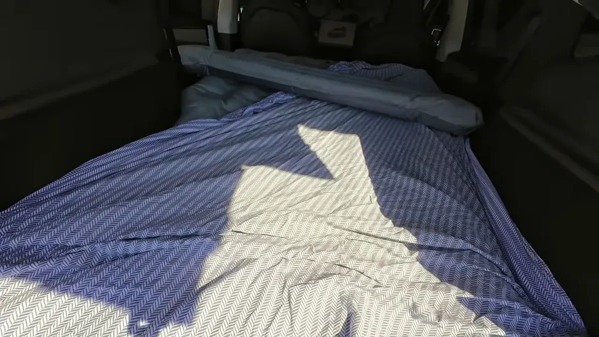 Grey and white herringbone-pattern bed sheet spread flat over the inflated air mattress inside a Tesla trunk