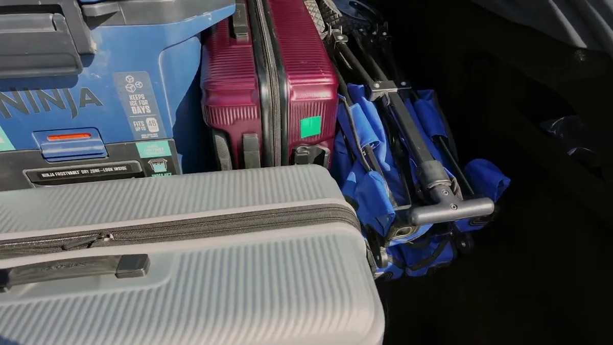 Tesla Model S trunk fully loaded with two suitcases and a folded utility cart.