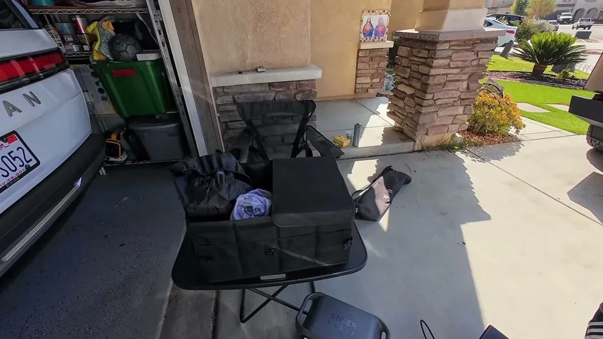 Close-up of black multi-compartment trunk organizer loaded with camping accessories next to Tesla Model Y