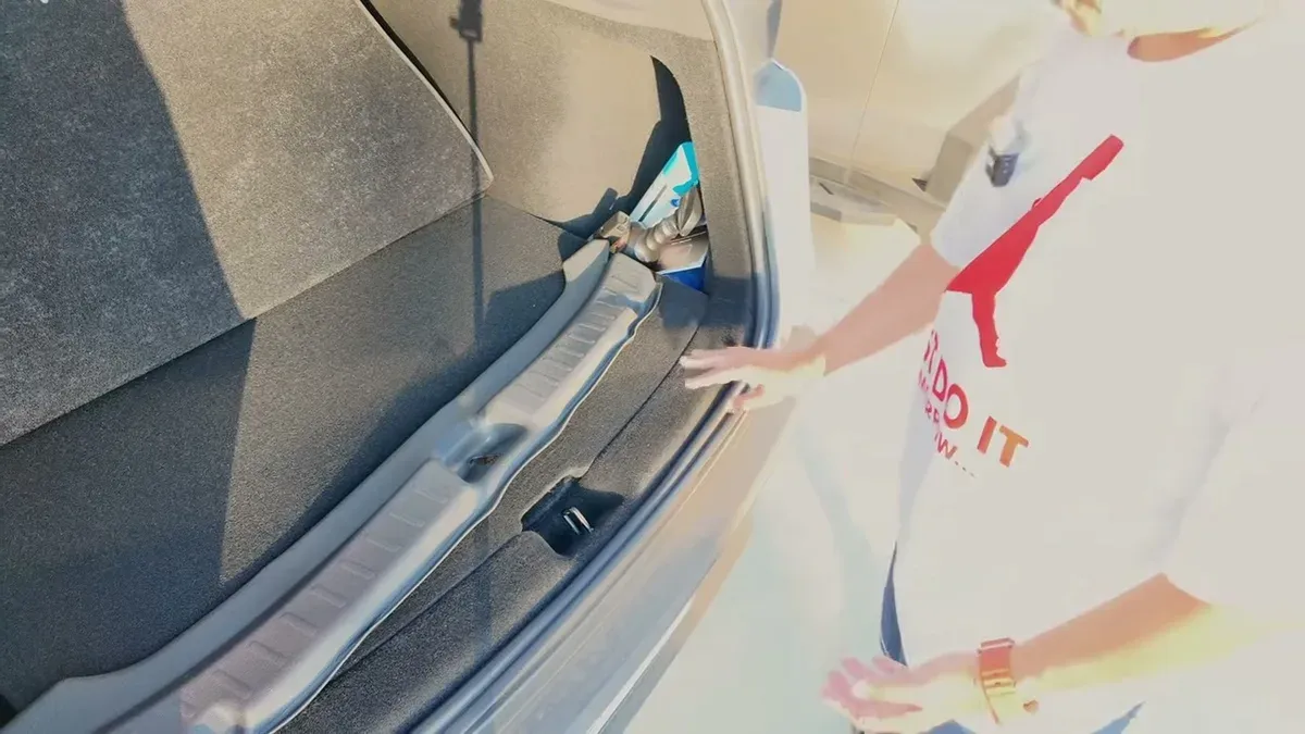 Hand pointing to trunk sill protection mat in a white Tesla's open trunk.