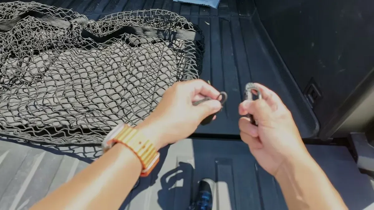 Hands attaching the BestEVMod cargo net to an anchor point in the Cybertruck bed