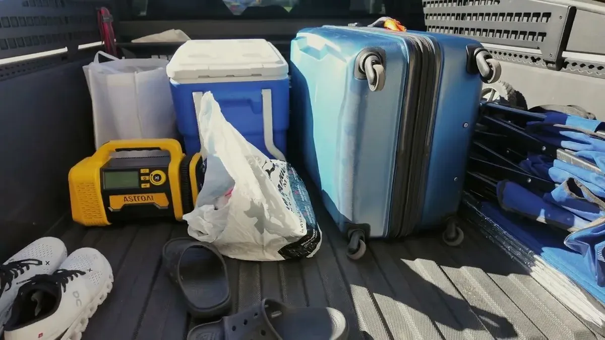 Truck bed packed with blue suitcase, cooler, portable power station, and travel gear.
