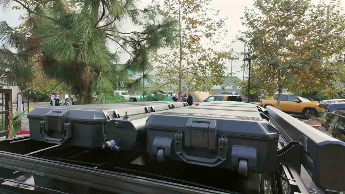 Close-up of two black Pelican Vault cases on the roof rack, pine trees visible in the background