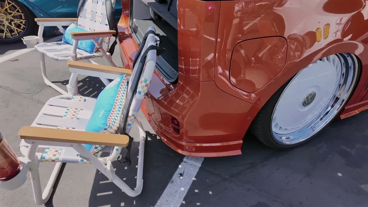 Rear-quarter view of the orange VW ID. Buzz with beach chairs and a teal Tesla Model 3 in the background