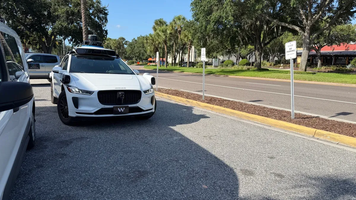 A white Waymo self-driving Jaguar I-Pace parked on a sunny Orlando street lined with palm trees.