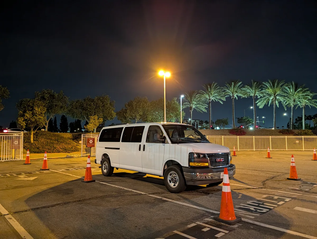 White GMC Savana van in a dark parking lot at night, orange cones and palm trees in the background