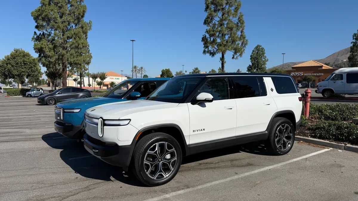White Rivian R1S and blue Rivian R1T parked in a sunny SoCal shopping center lot.