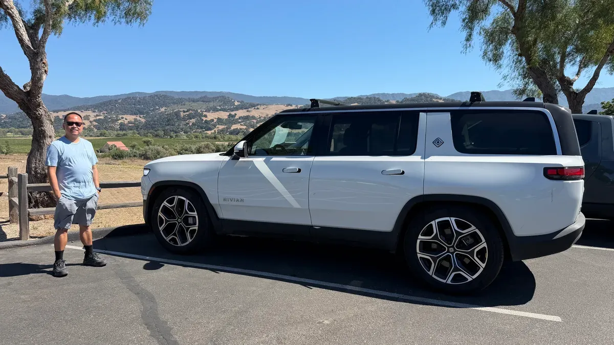 White Rivian R1S with a black roof parked at a valley overlook with vineyards and hills behind it