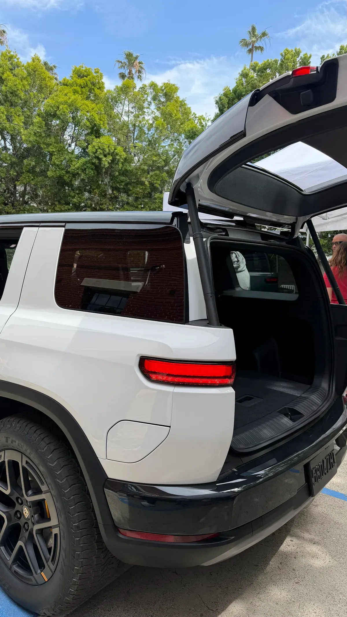 Close-up of white Rivian R2 rear with trunk open, showing the distinctive horizontal taillight bar.