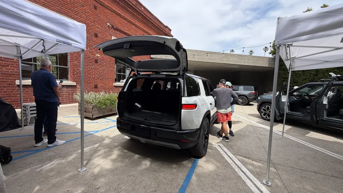 White Rivian R2 SUV with open trunk at the Venice outdoor event, crowd gathering around.